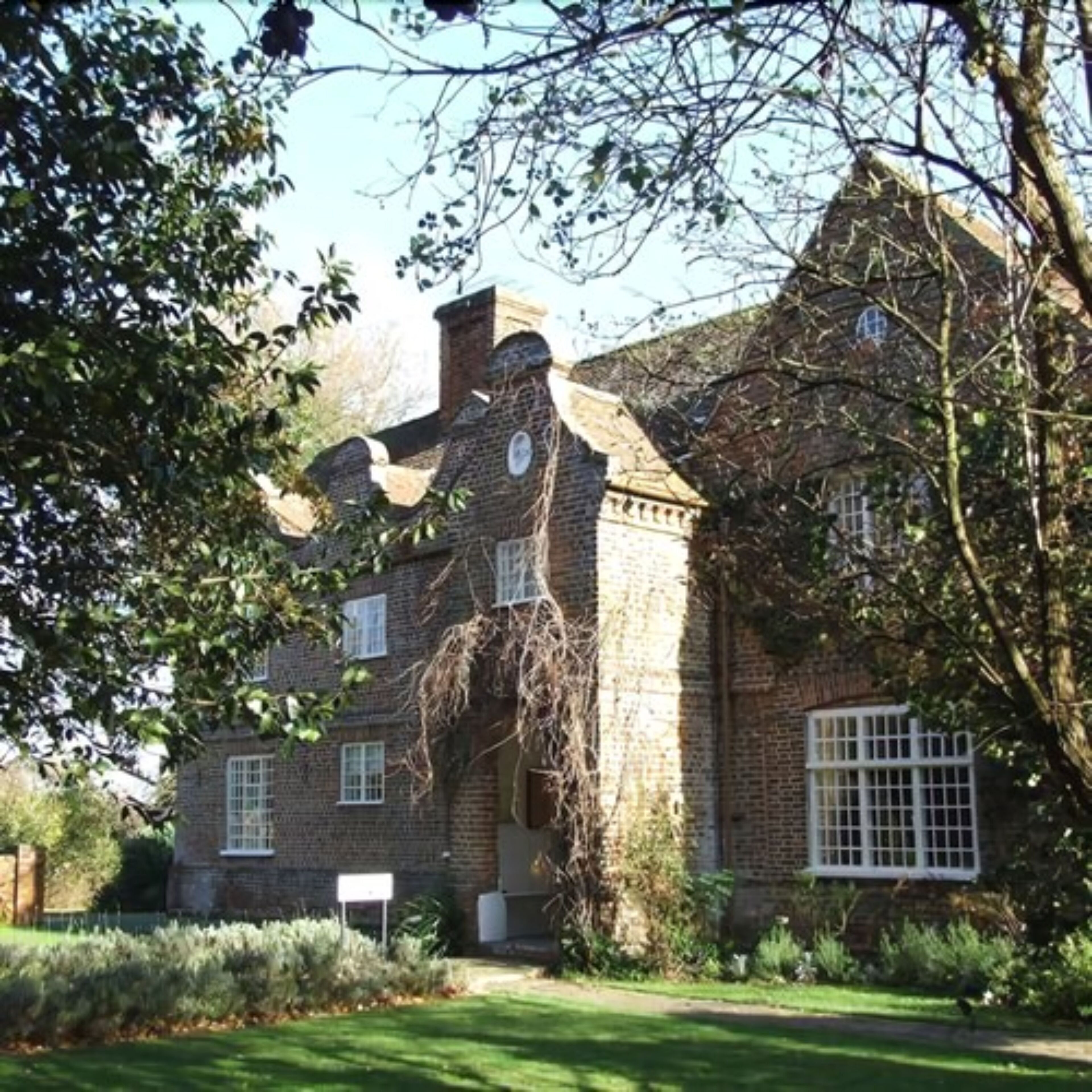 A traditional brick house with a prominent chimney, a large window, and a well-maintained garden.
