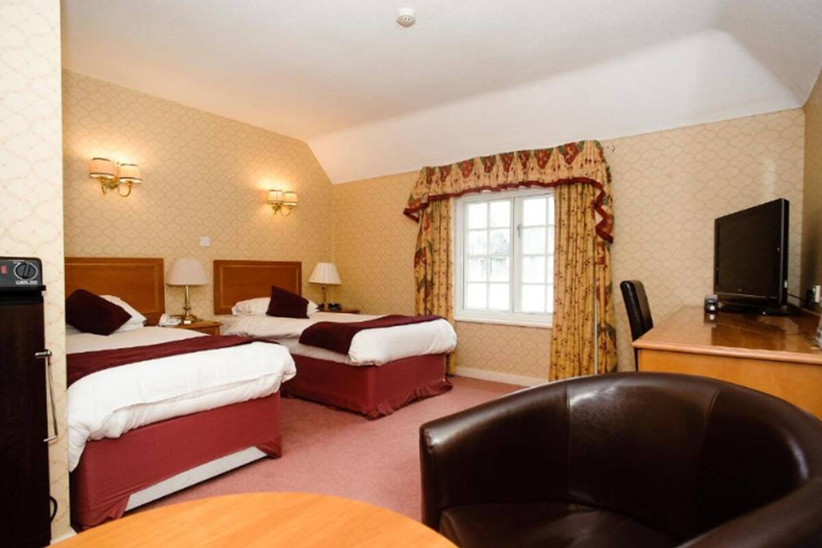 A hotel room with two beds, a desk, a television, and a leather chair.