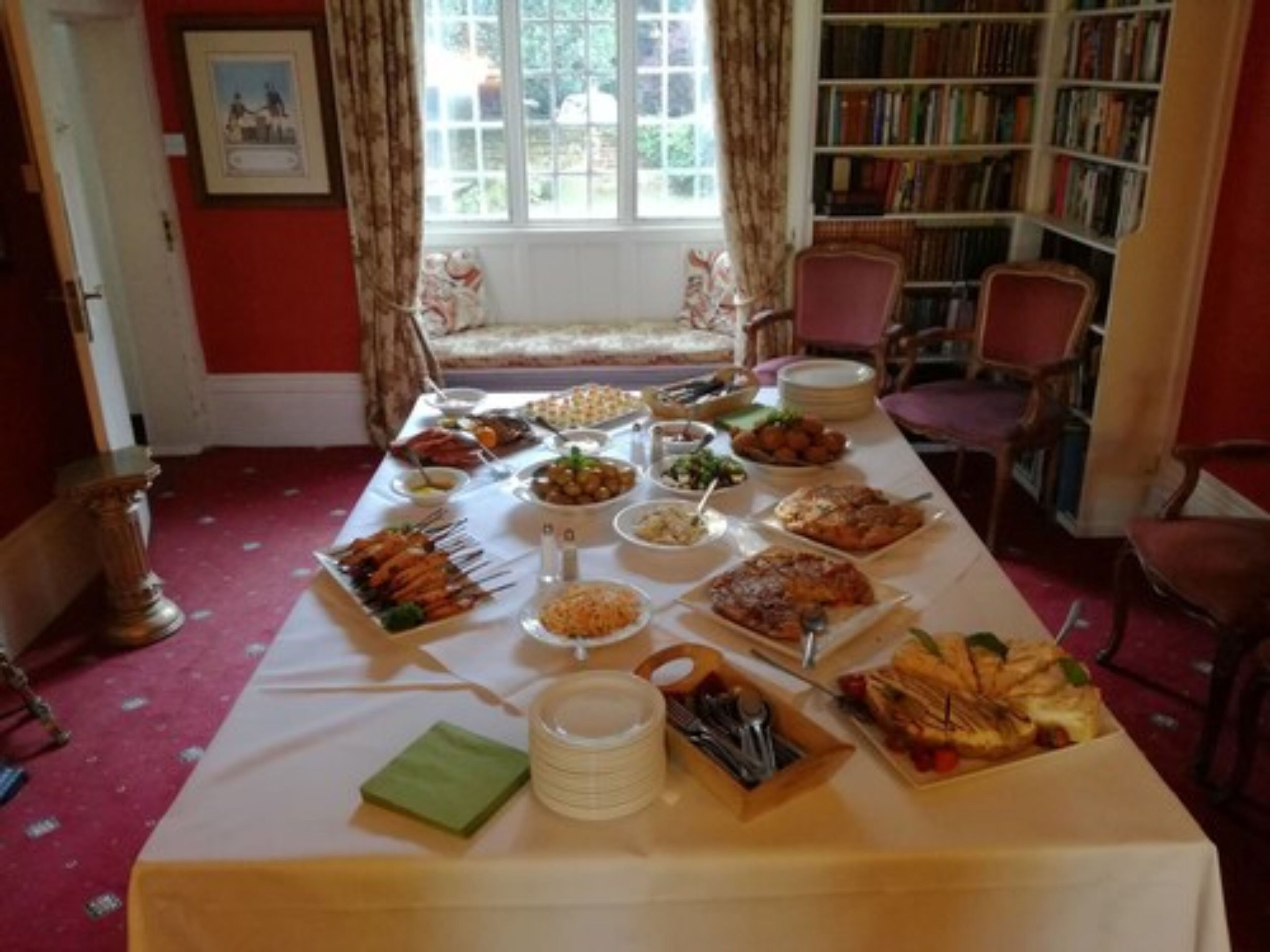 A dining table with various dishes, a bookshelf, and a window with curtains.