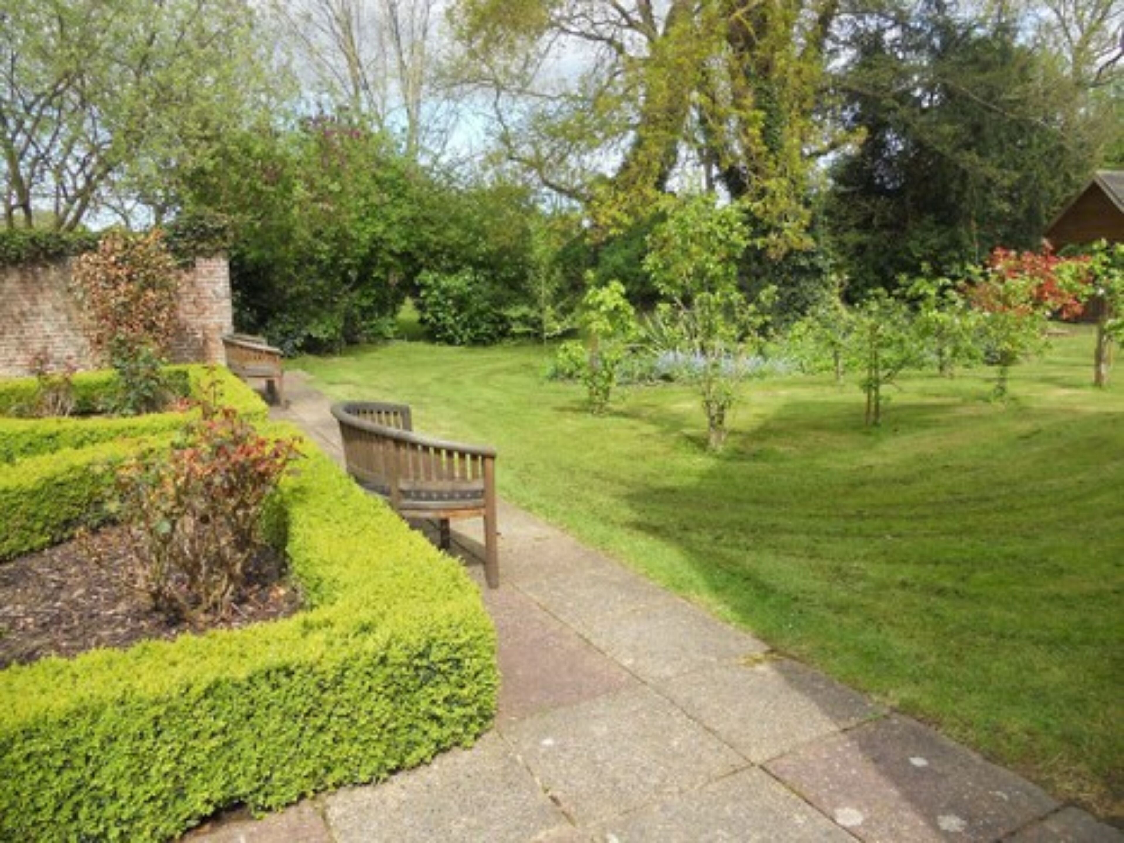 A well-maintained garden with a paved pathway, a wooden bench, and various shrubs and trees.