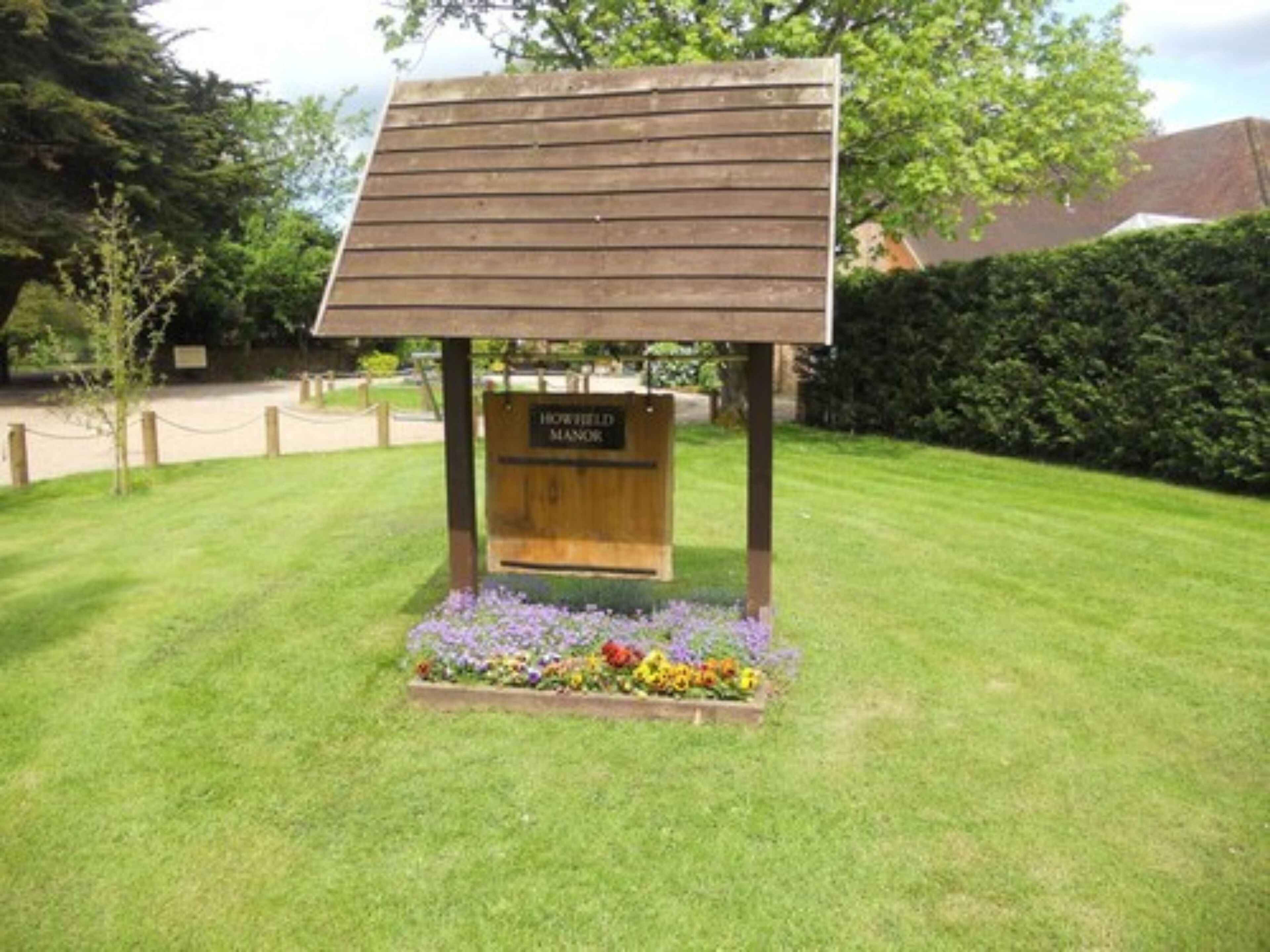 A wooden sign with the text "HOWFIELD MANOR" in a garden setting.