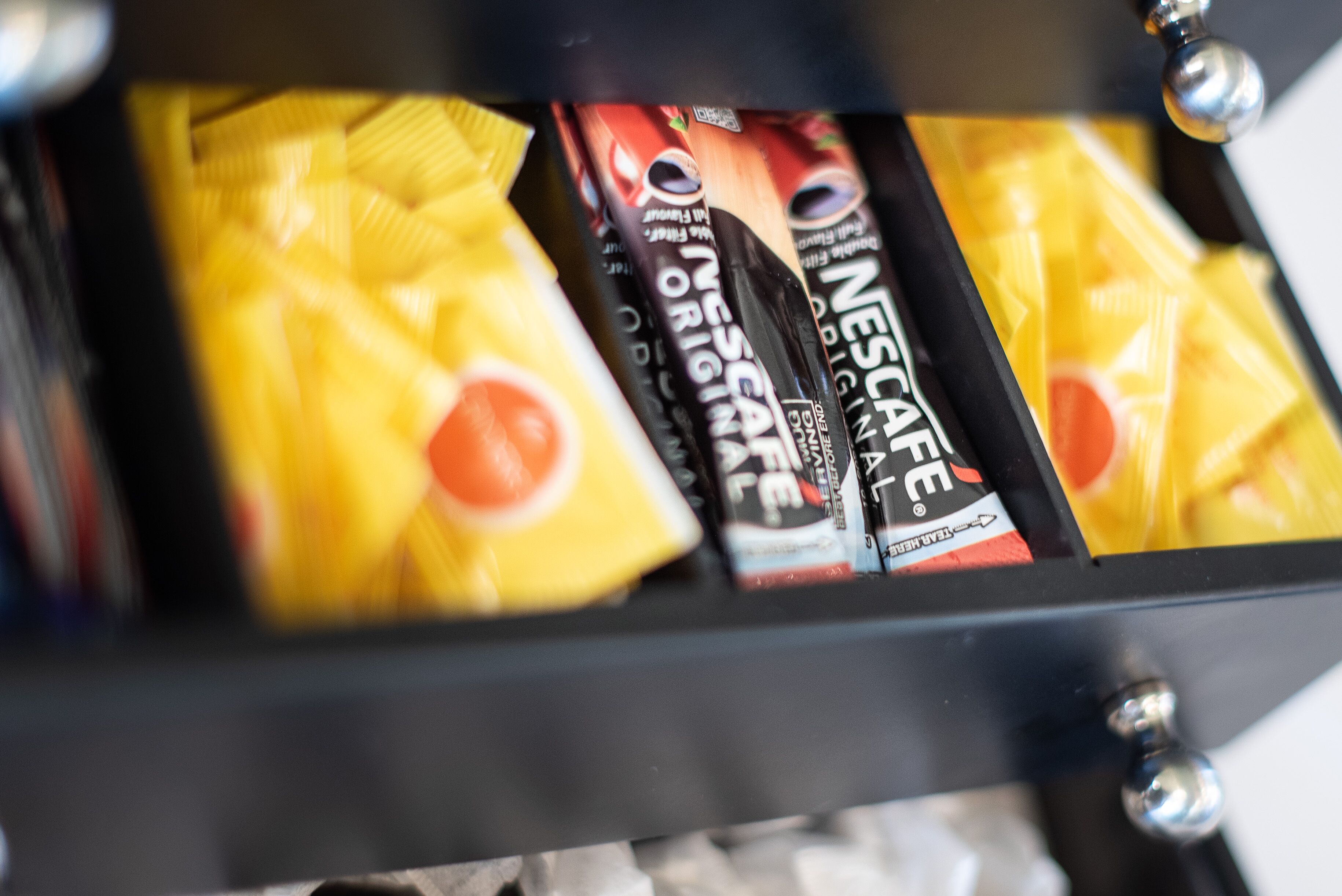 A drawer with multiple compartments containing various items, including a yellow bag and a black box labeled 'NESCAFE'.