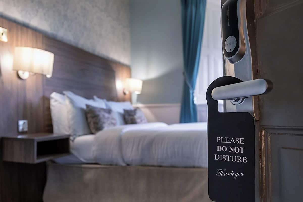 A hotel room with a bed, bedside lamps, and a door with a 'Please Do Not Disturb' sign.