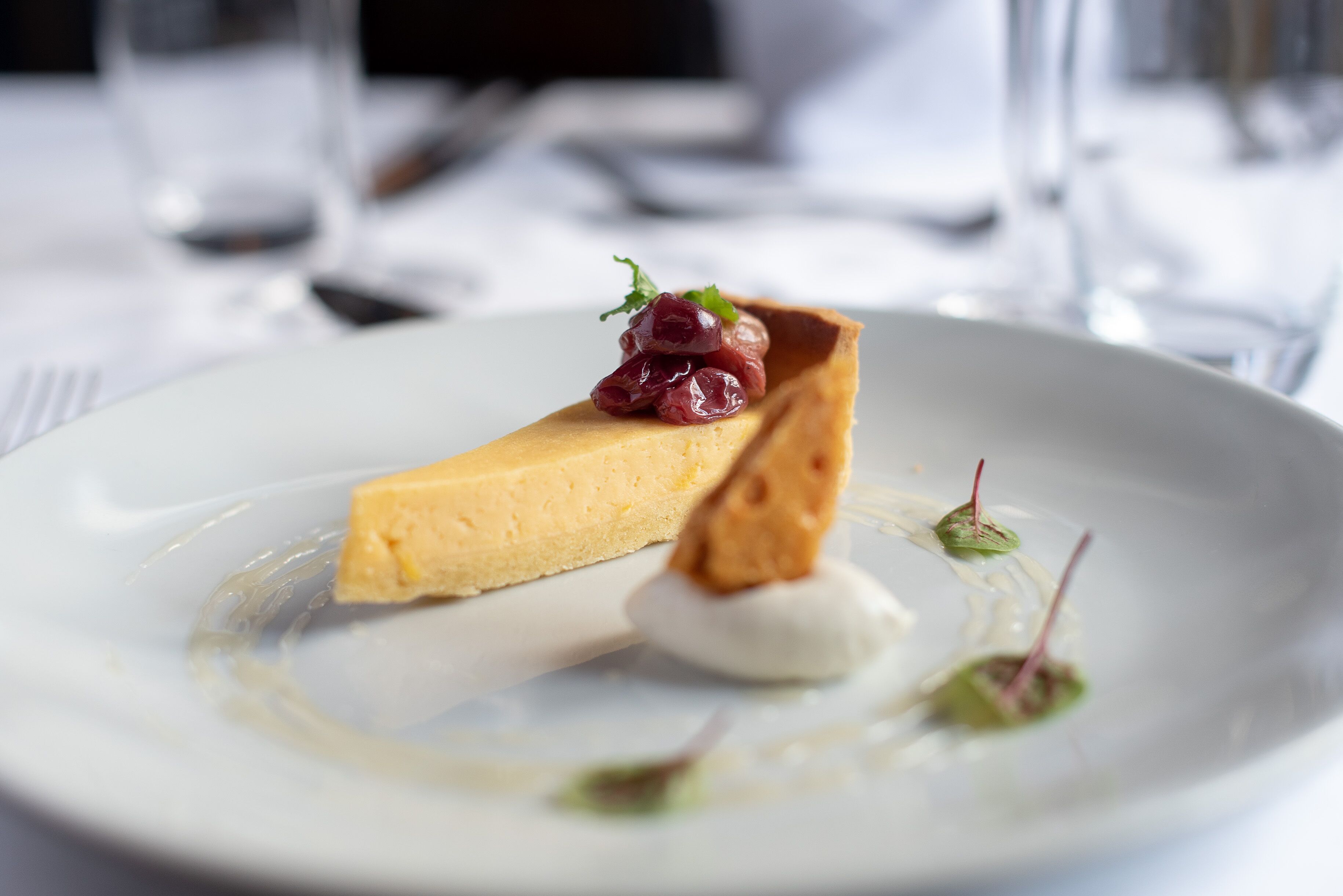 Een nagerechtenbord met een stuk cheesecake, een toefje slagroom en garnering.