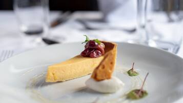 Een nagerechtenbord met een stuk cheesecake, een toefje slagroom en garnering.