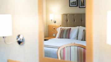 A hotel room with a bed, a nightstand, a wall-mounted lamp, and framed pictures on the wall.