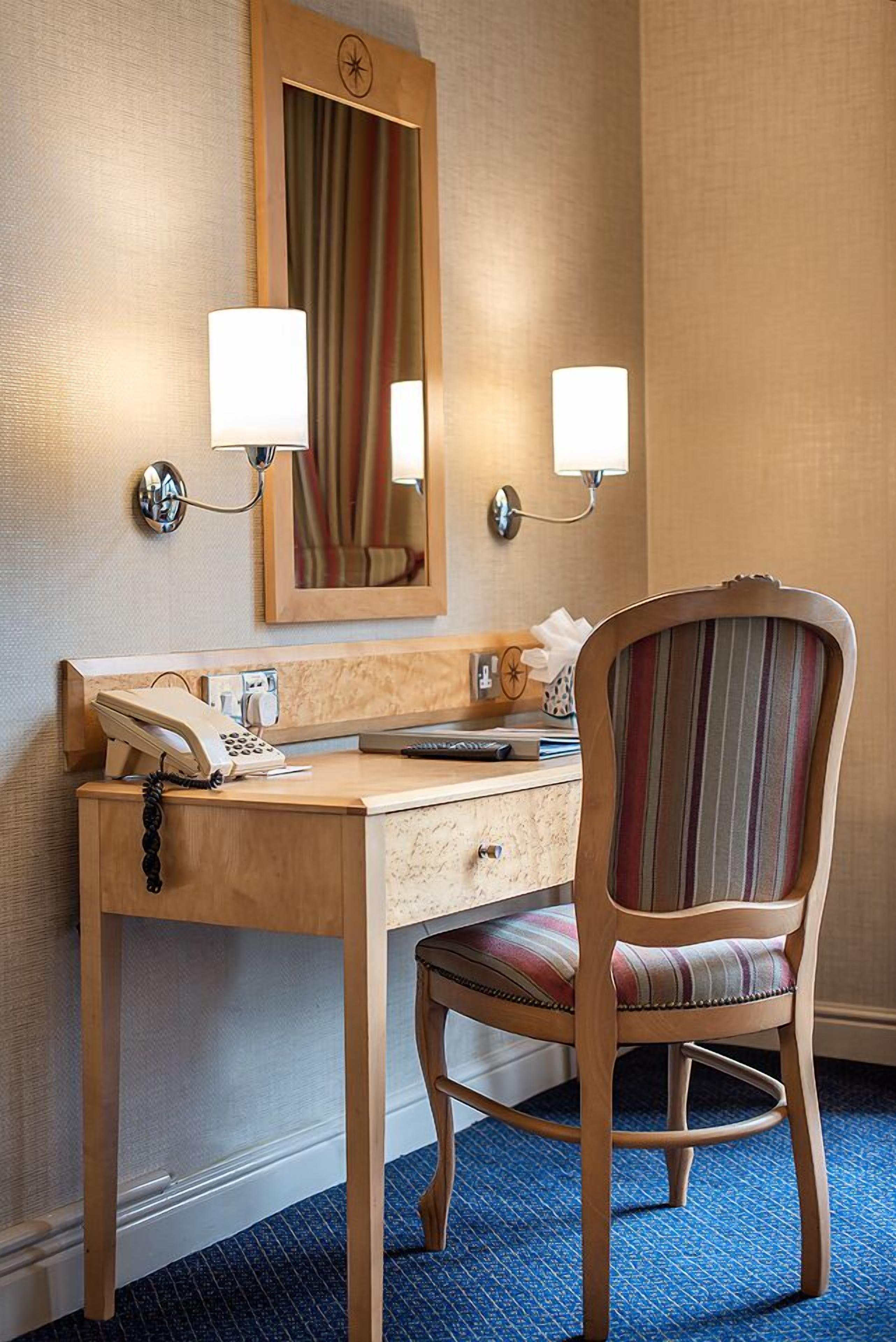 Une chambre d’hôtel avec un bureau en bois, un téléphone, un miroir et deux lampes fixées au mur.