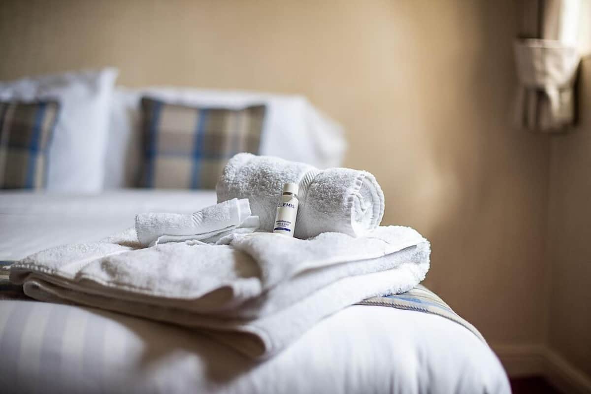 A neatly made bed with white linens and a bottle of toiletries on it.