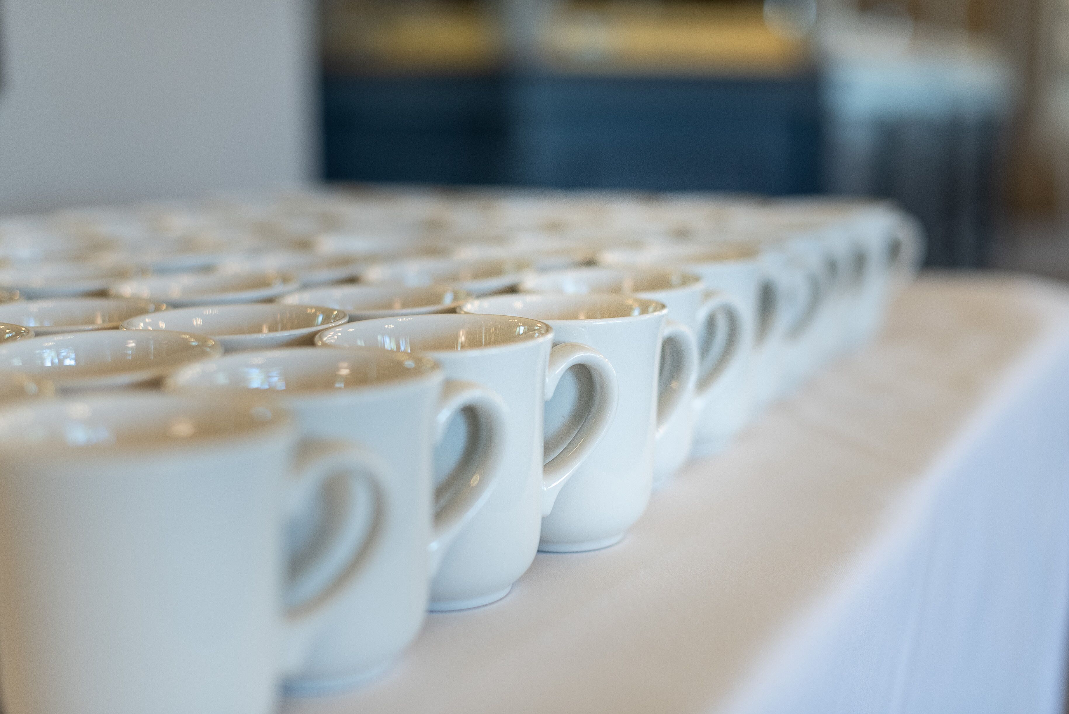 A row of white ceramic cups with handles, arranged on a table.