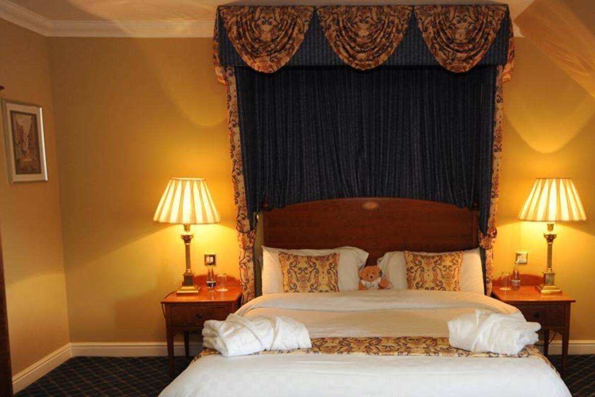 A hotel room with a large bed, two bedside lamps, a dark curtain, and a wooden headboard.