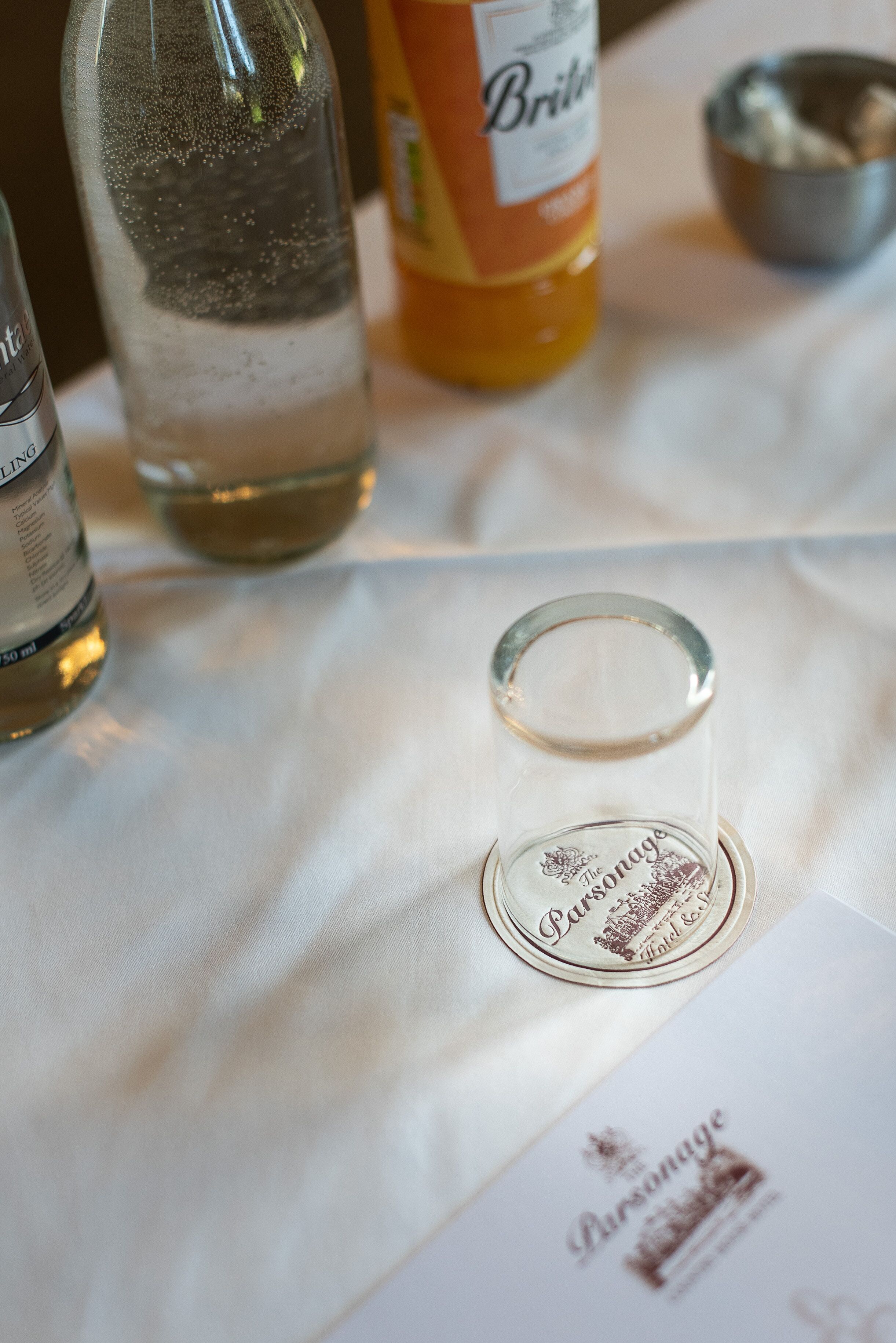 A table with a bottle of Brienne, a glass bottle, and a small glass container on a white tablecloth.