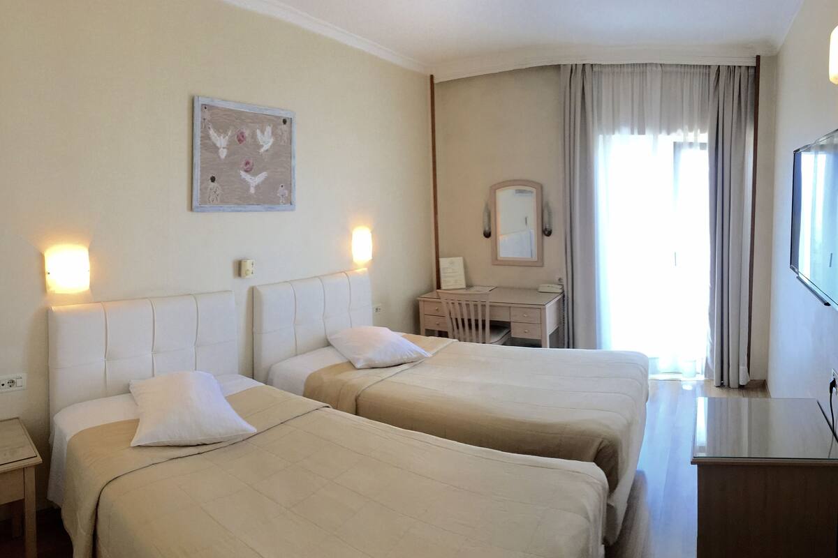 A hotel room with two beds, a desk, a chair, a TV, and a painting on the wall.