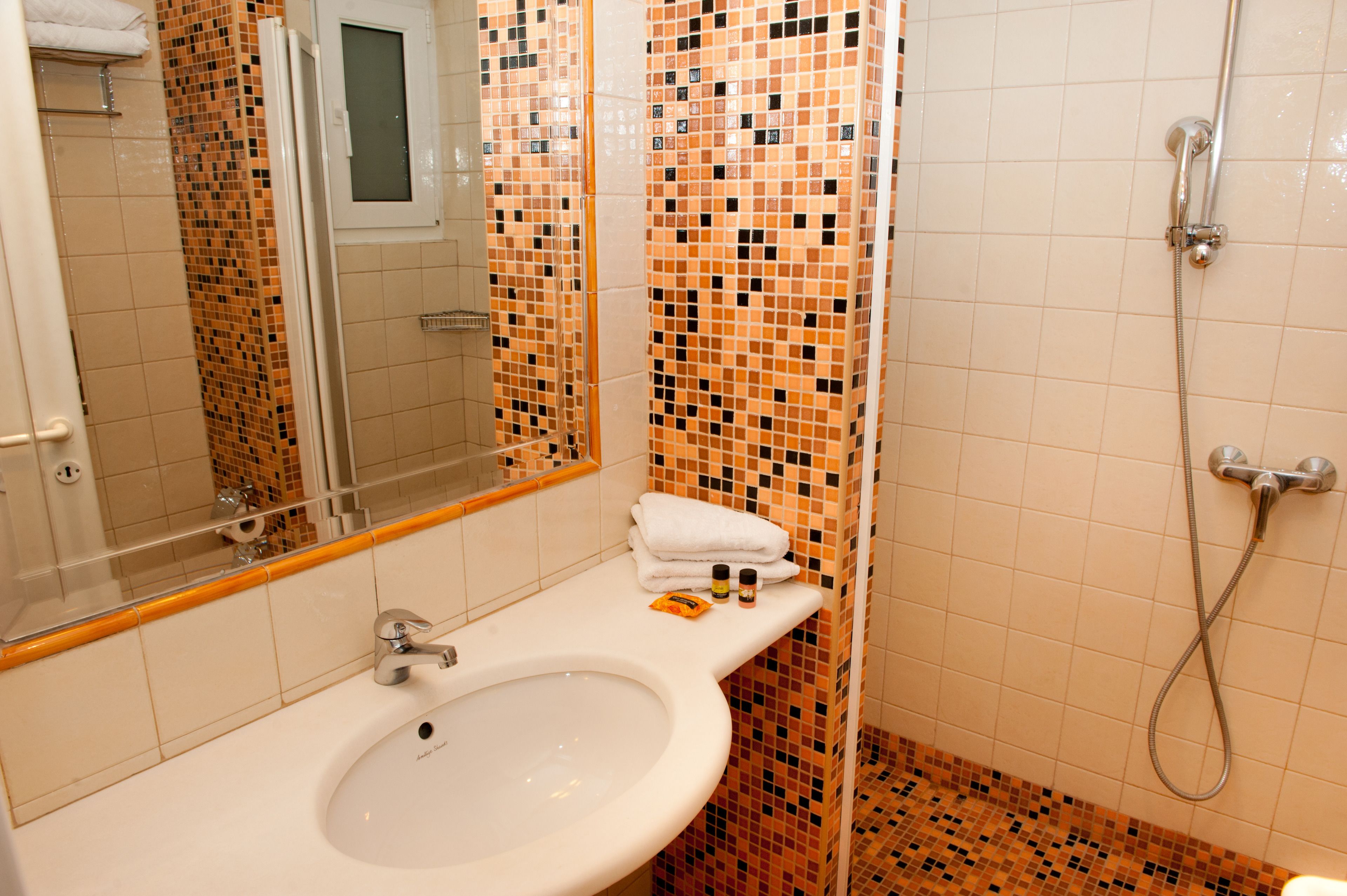 A bathroom with a white sink, a mirror, and a shower area with mosaic tiles.
