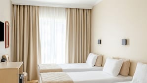 Una habitación de hotel con dos camas, un escritorio y un amplio ventanal con cortinas.