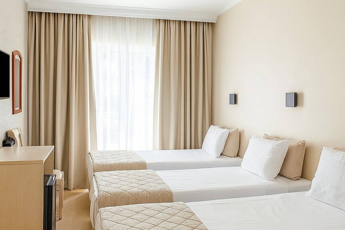 A hotel room with two beds, a desk, and a large window with curtains.