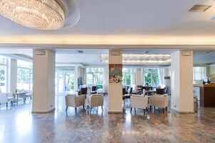 Eine geräumige Hotelhalle mit hoher Decke, großen Fenstern und einem zentralen Kronleuchter.