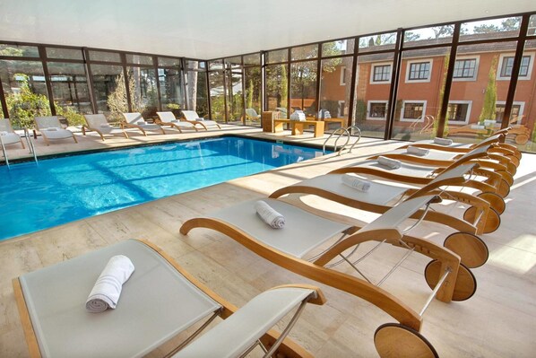 Un espace aménagé au bord de la piscine, avec des chaises longues et une piscine, le tout entouré de grandes fenêtres offrant une vue sur le bâtiment et la verdure.