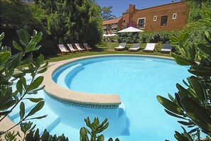 Une piscine avec des chaises longues et, en arrière-plan, un bâtiment en briques.