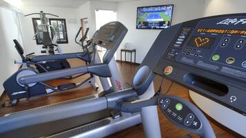 Un gimnasio con cintas de correr, elípticas y una pantalla digital para datos del entrenamiento.