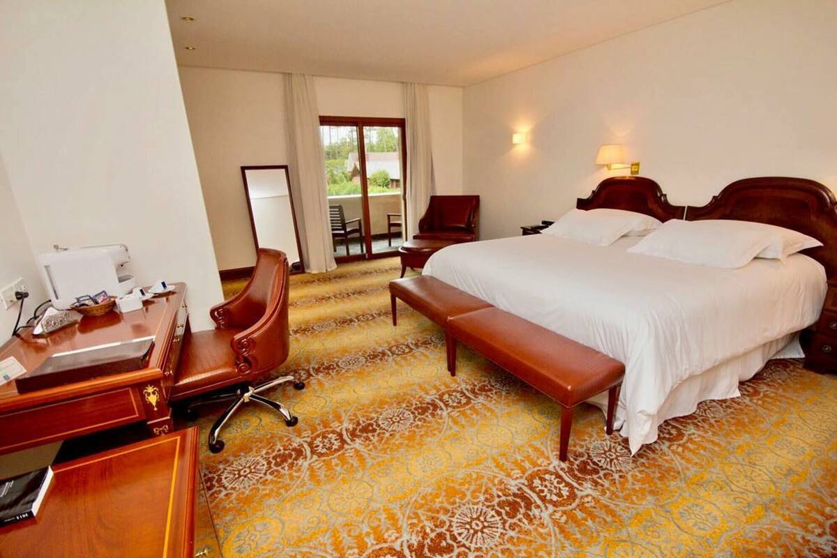 Une chambre d’hôtel avec un grand lit, un bureau avec un téléphone, une chaise et un banc.