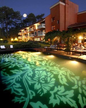 Un hôtel doté d’une piscine ornée d’un motif de feuilles vertes, d’un espace extérieur aménagé et offrant une vue sur le ciel nocturne et la lune.