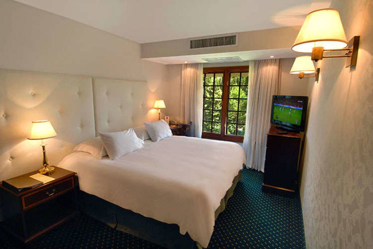 Une chambre d’hôtel avec un grand lit, deux lampes de chevet, une télévision et une fenêtre avec des rideaux.