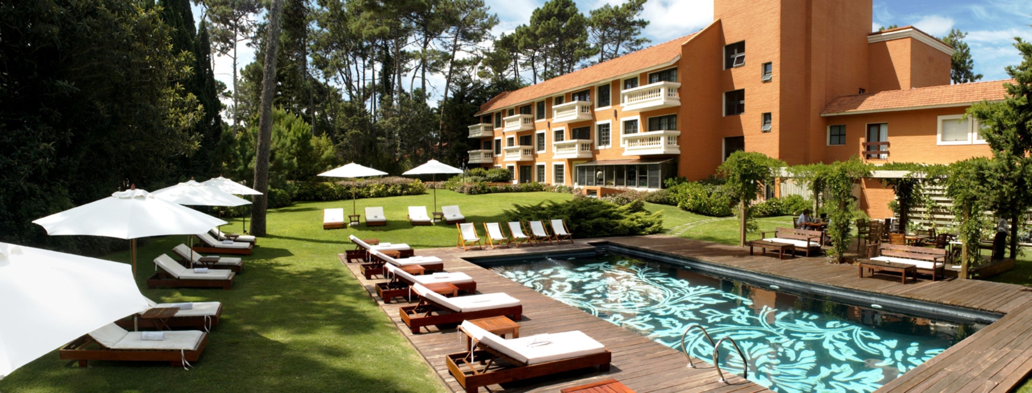 A pool area with lounge chairs and umbrellas, surrounded by a well-maintained lawn and a multi-story building with balconies.