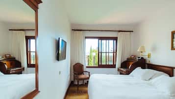 A hotel room with two beds, a television, a desk with a lamp, and a chair.