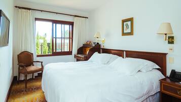 Une chambre d’hôtel avec un grand lit, une chaise, une table de chevet, une lampe et une fenêtre avec des rideaux.