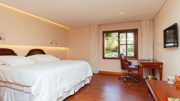 Habitación de hotel con una cama grande, un escritorio y una silla. Se ve un paisaje verde a través de la ventana.