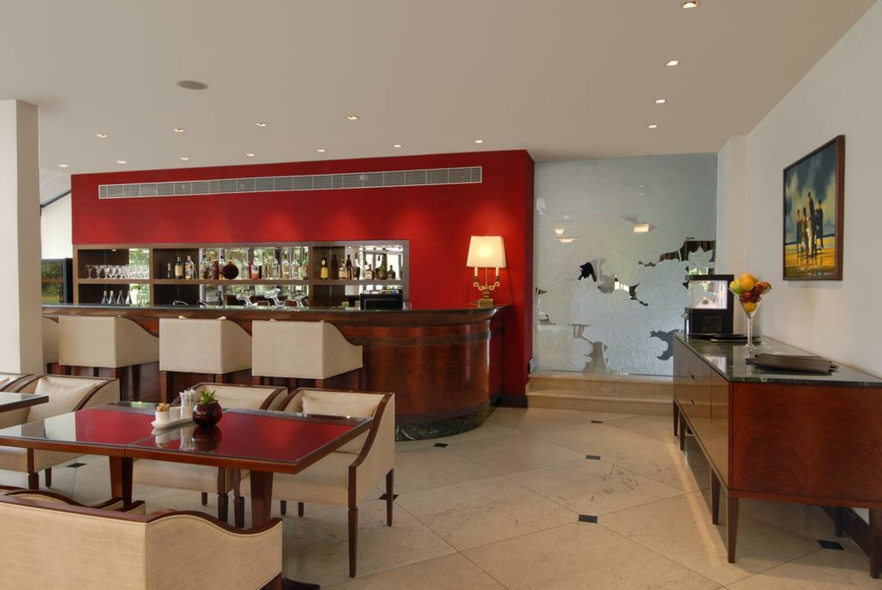 Un área de bar moderna con una pared de acento roja, una barra y una zona de estar con mesas y sillas.