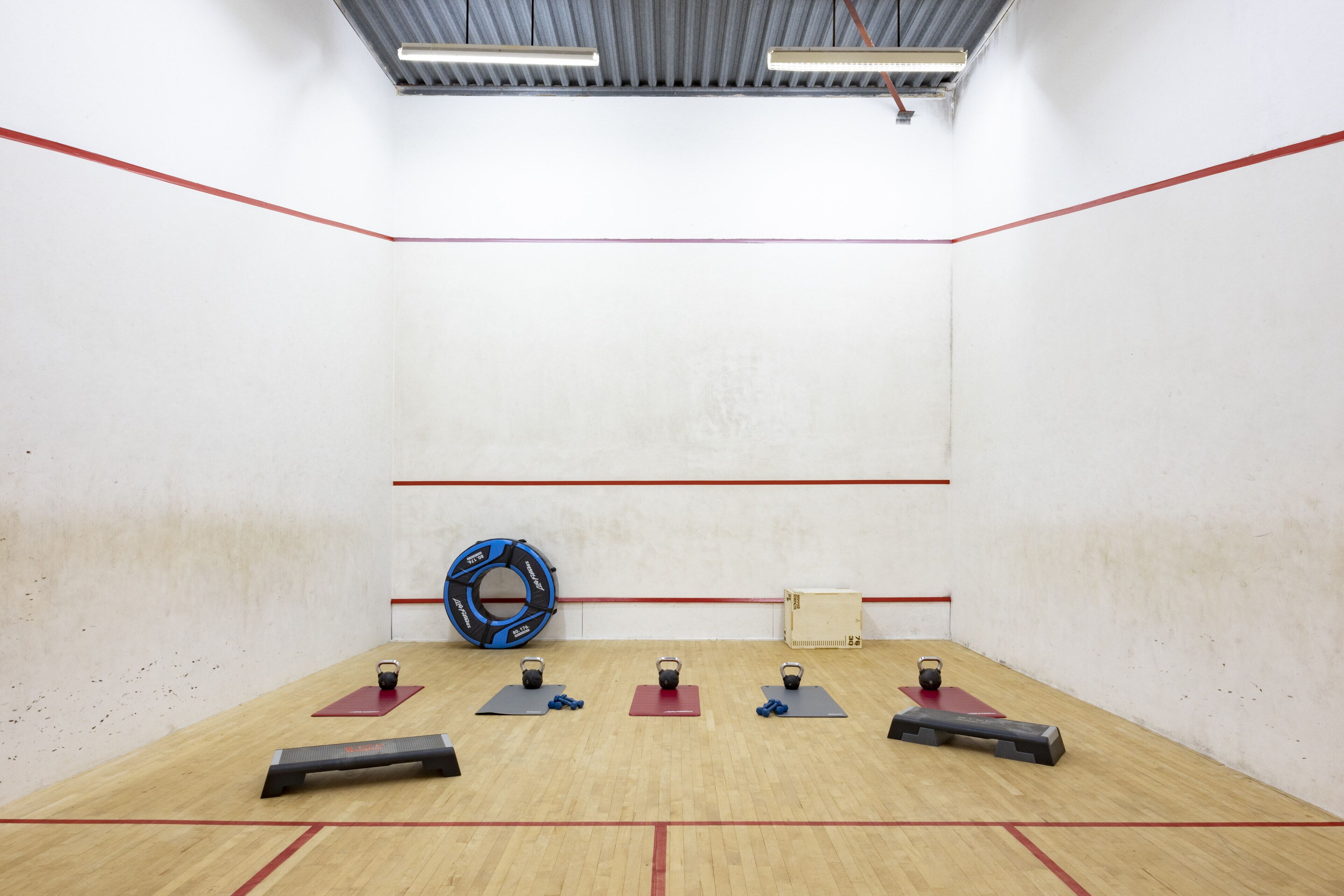 Una cancha de squash con piso de madera, líneas rojas que delimitan el campo y equipo de ejercicio.