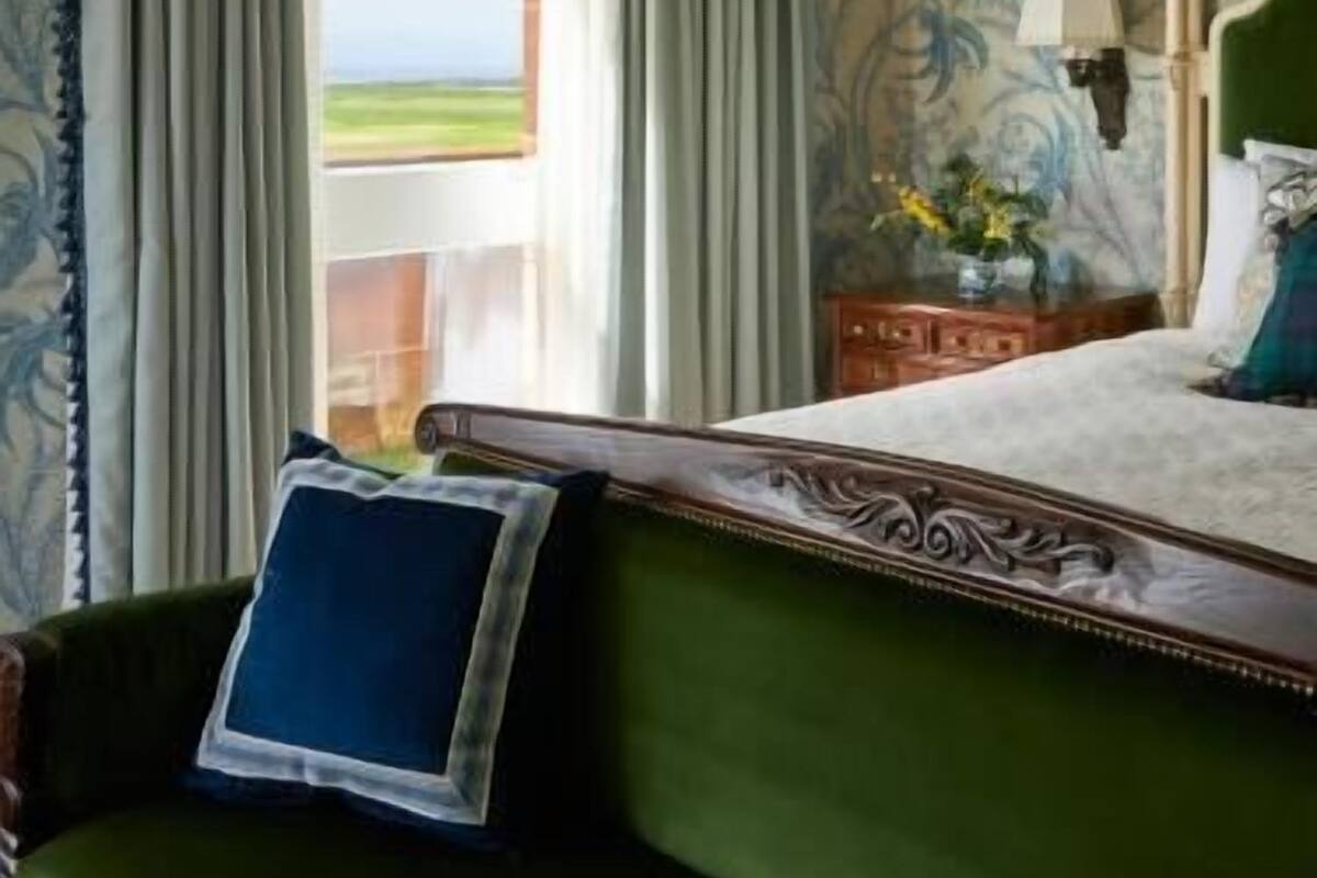 A room with a bed, a green sofa, a window with curtains, and a wall with a floral pattern.