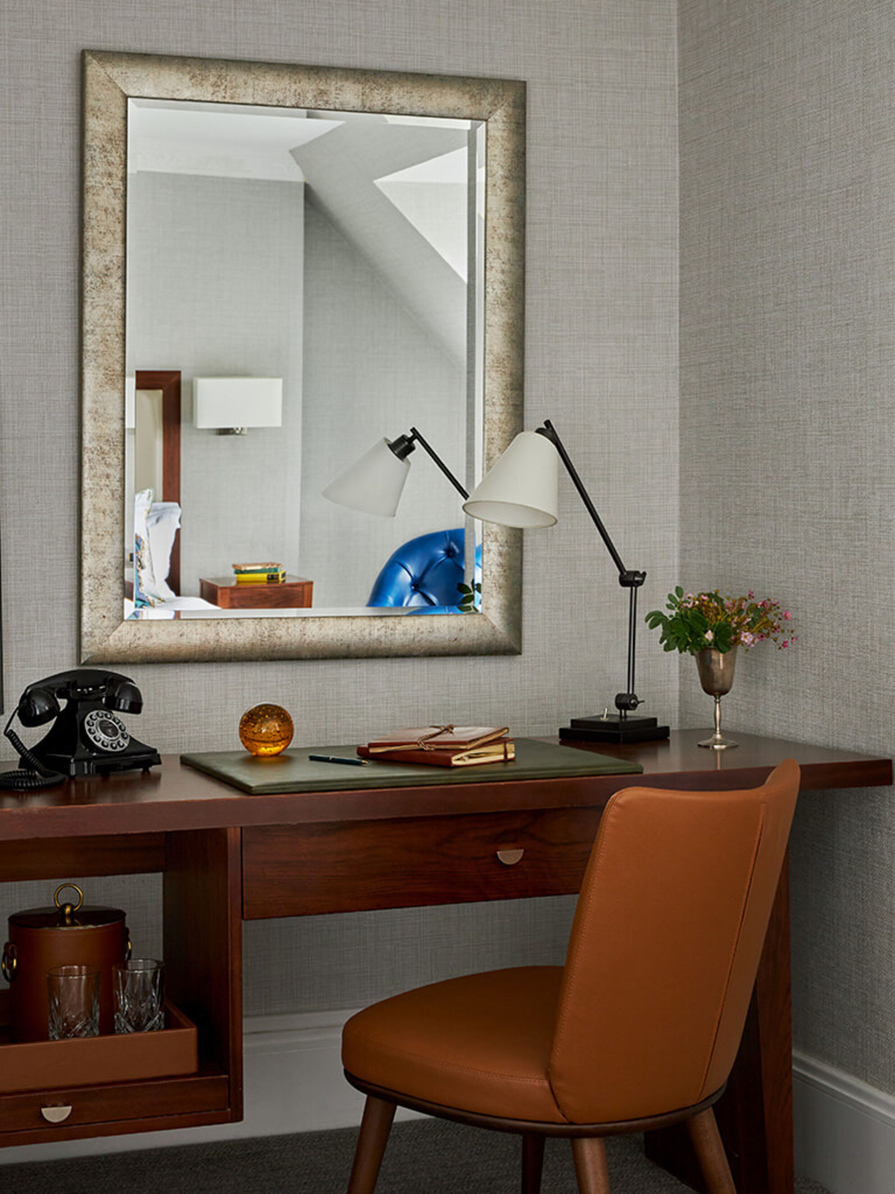 A desk with a mirror, a lamp, a chair, and a small plant.