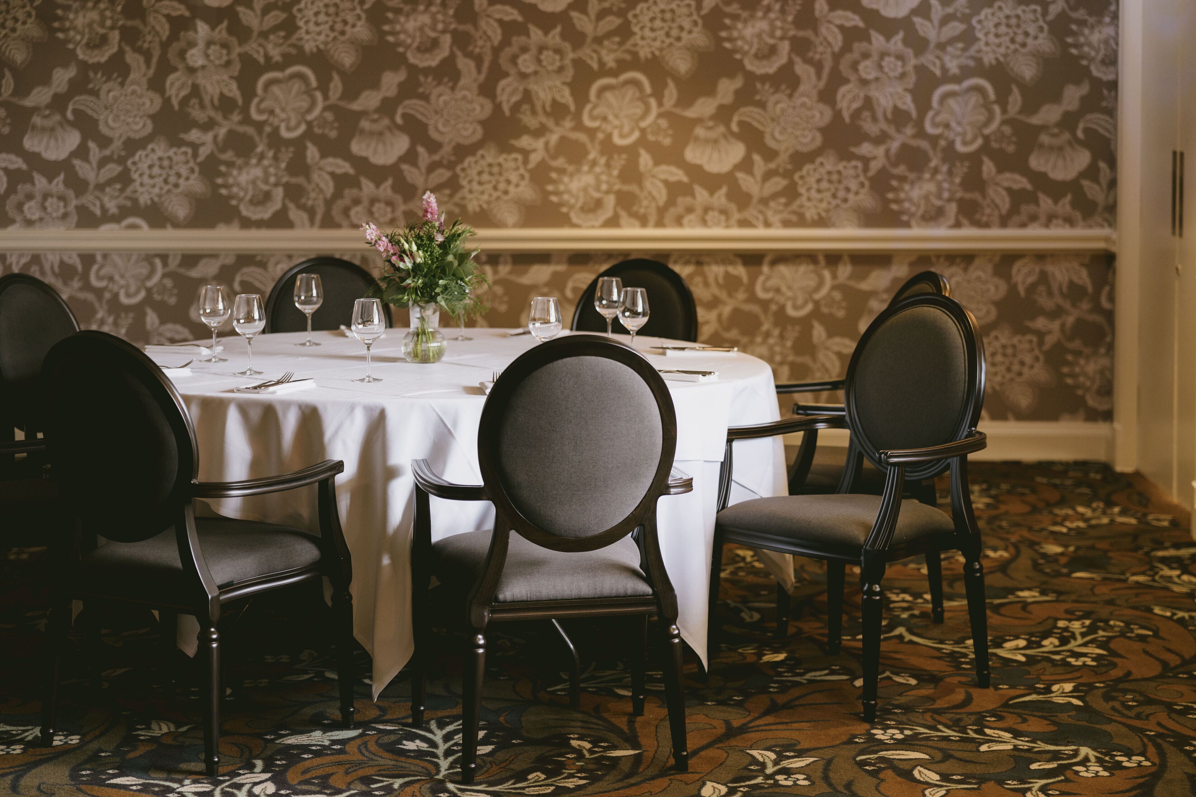 A dining table set for six with chairs, a vase with flowers, and a patterned carpet.