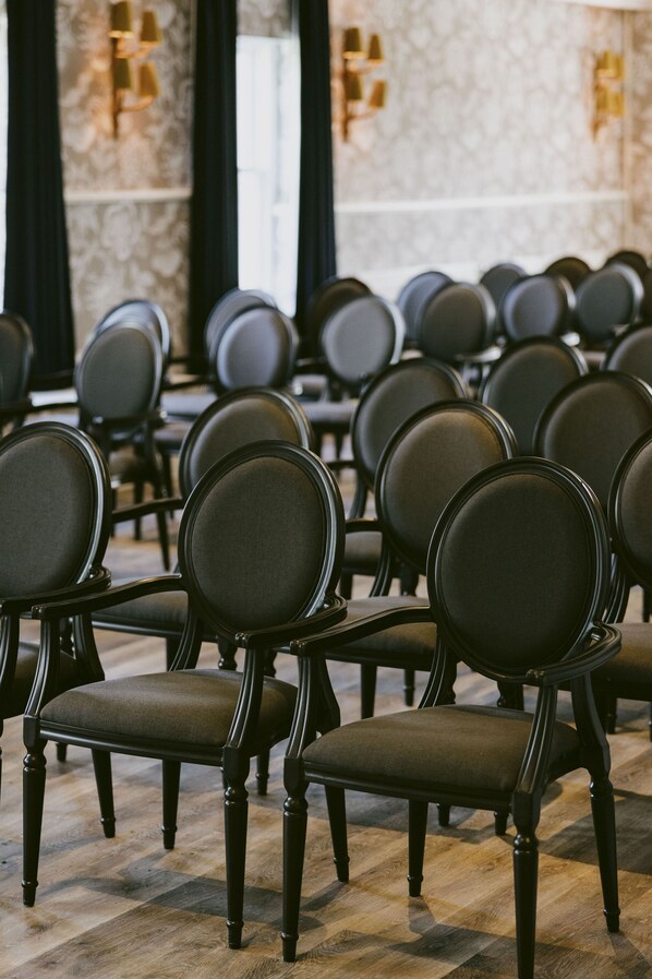 Filas de sillas de madera oscura con asientos y respaldos acolchados, dispuestas en una sala de conferencias con piso de cuadros y paredes de mármol.