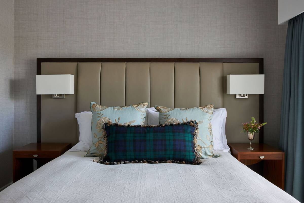A neatly made bed with a patterned pillow, two bedside tables with lamps, and a vase with flowers.