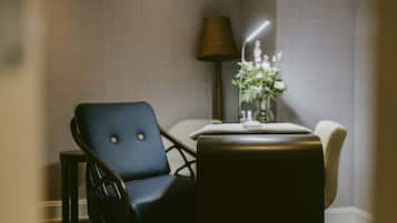Et værelse med en mørkeblå stol, et lille bord med en lampe og en vase med blomster.