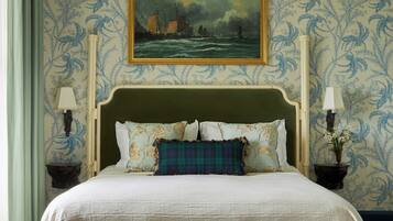 A bed with a green headboard, white bedding, and a plaid pillow. There is a painting above the bed and two bedside tables with lamps.