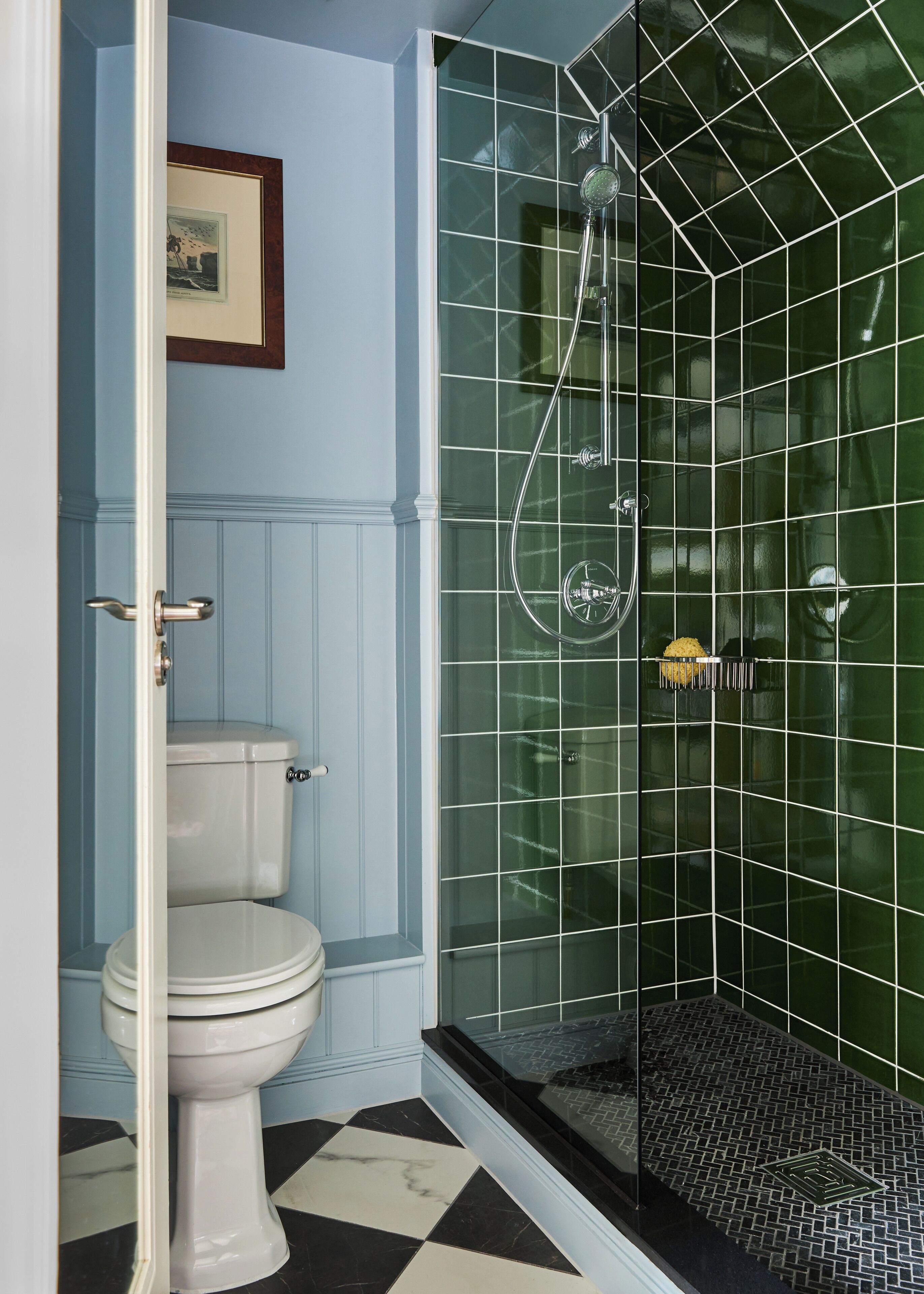 A bathroom with a white toilet, a glass-enclosed shower with a black floor, and green tiled walls.