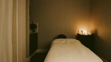 A dimly lit room with a bed, a nightstand with a lamp, and a small cabinet.