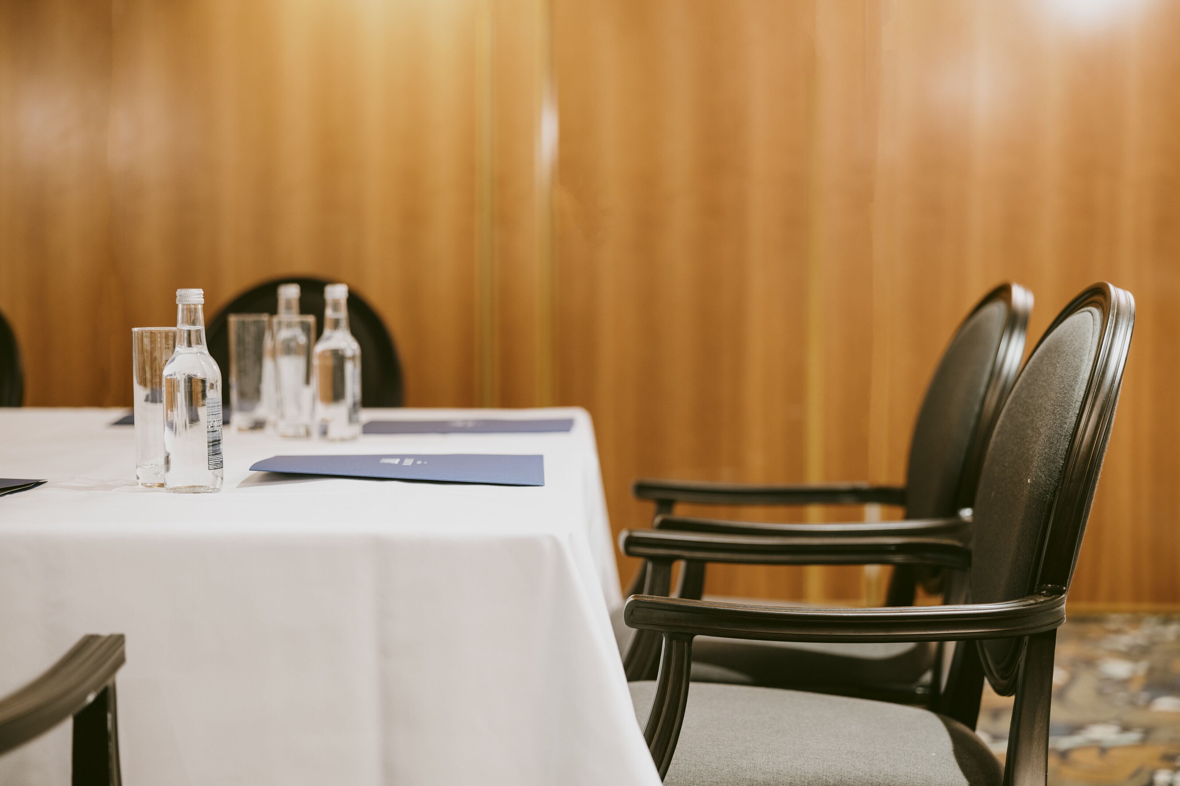 Une table de conférence avec des bouteilles d’eau, un dossier bleu et une nappe blanche.