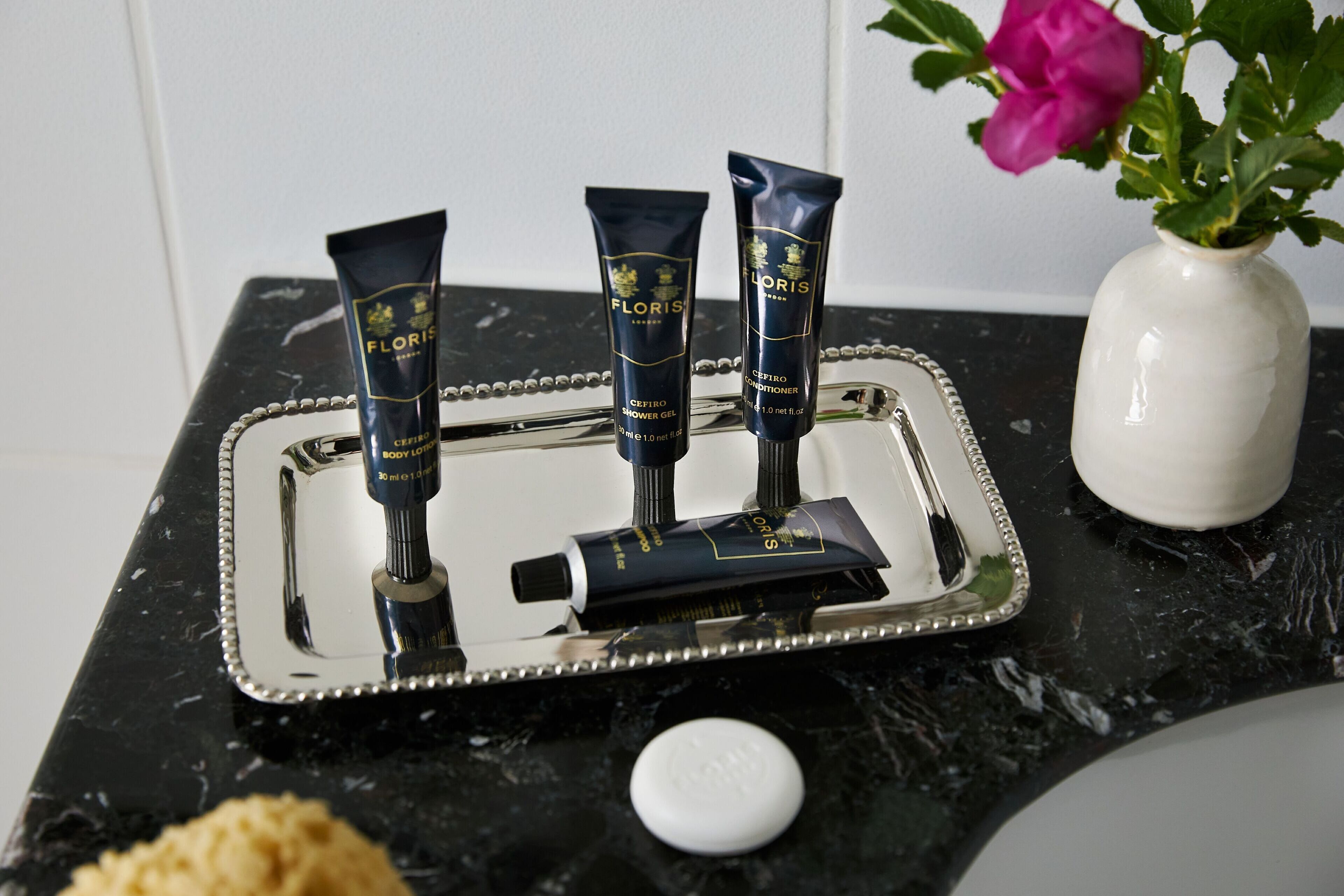A tray with three tubes of shower gel and a bar of soap on a marble countertop.