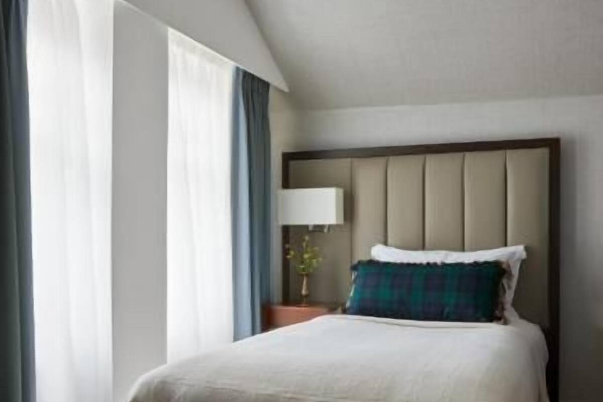A hotel room with a large bed, a nightstand, a lamp, and a window with curtains.