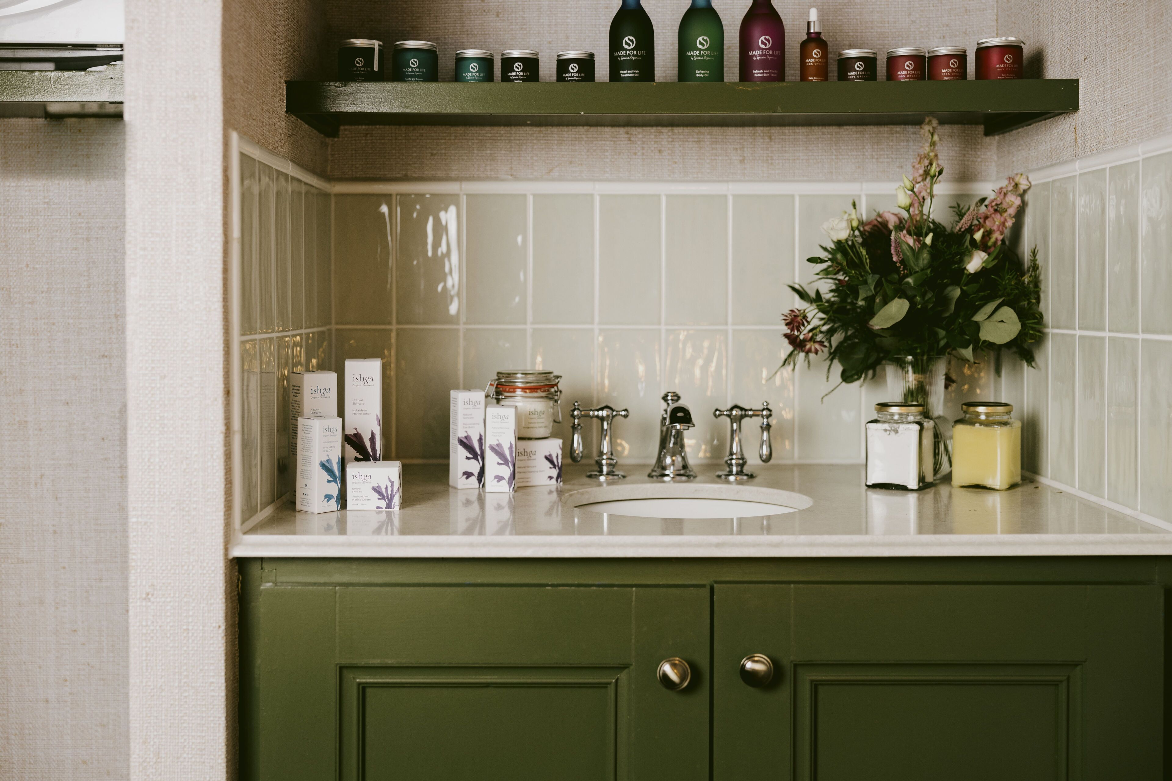 Una cocina con un armario verde, un lavabo blanco y varios frascos y botellas en un estante sobre el lavabo.