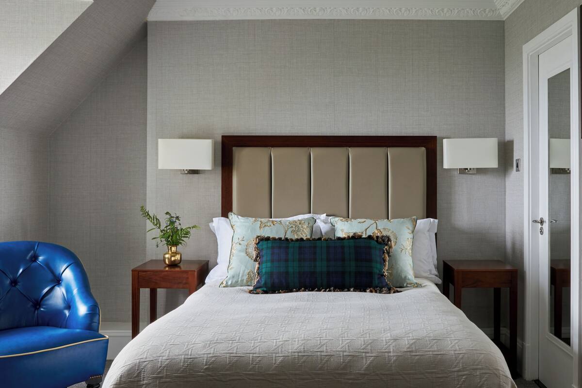 A bedroom with a large bed, two bedside tables, a blue armchair, and a door.