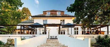 Una casa señorial con una escalera central que conduce a un patio cubierto con mobiliario exterior.