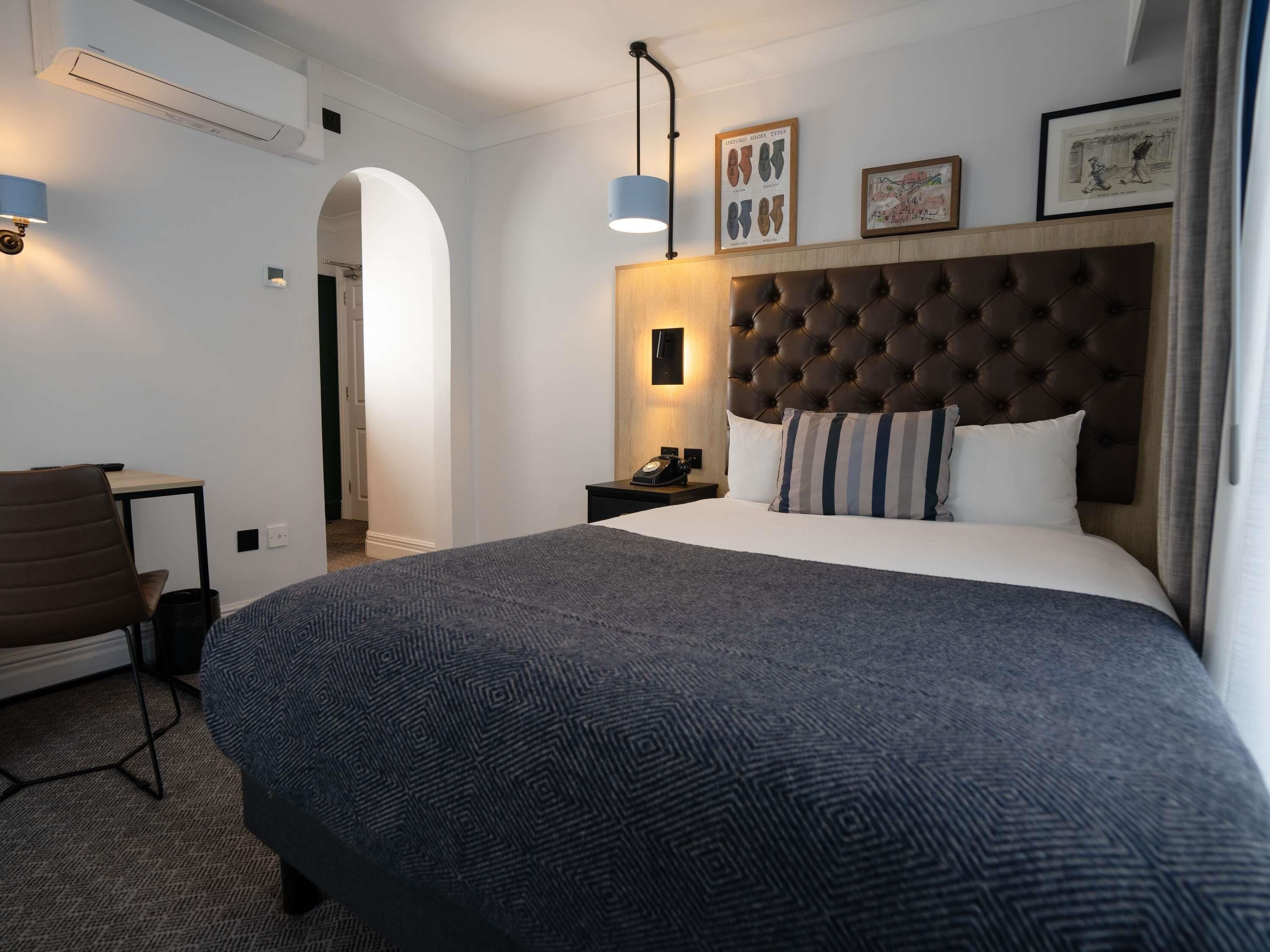 Ein Hotelzimmer mit einem großen Bett, einem Schreibtisch, einem Sessel, einem Nachttisch mit Lampe und einer Wand-Klimaanlage.