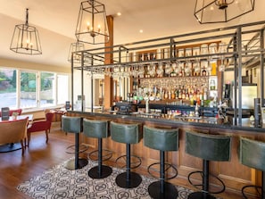 Zona de bar con taburetes, una barra llena de botellas y vistas al exterior.