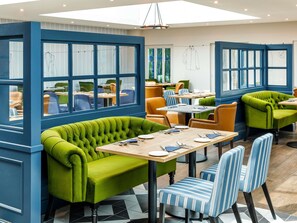 Ein Restaurant mit grün gepolsterten Sitzecken, gestreiften Stühlen und blauen Wänden.